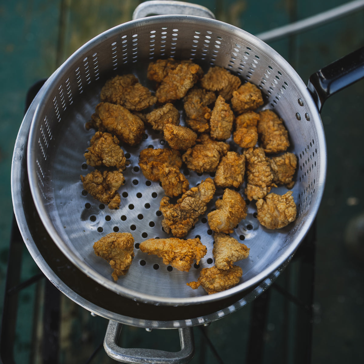 Fried chicken pieces in an aluminum fry pot on an outdoor cooker
