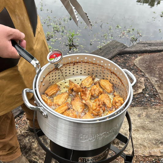 Man frying chicken wings in a fry pot over a single burner