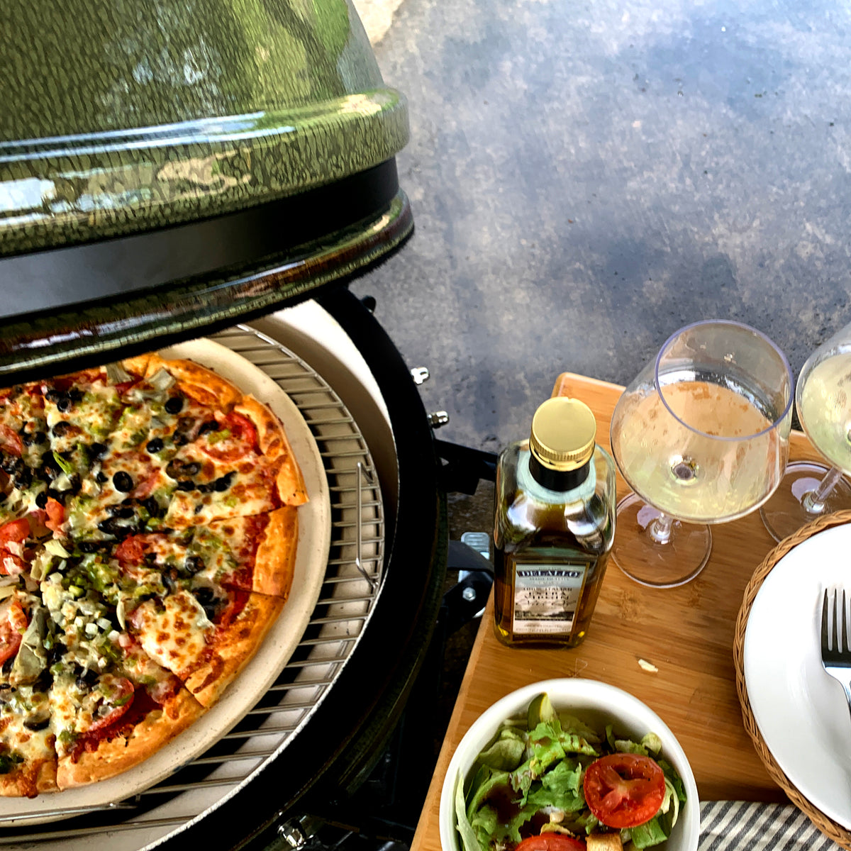 ceramic grill open with grilled pizza and ingredients sitting on a wood side shelf