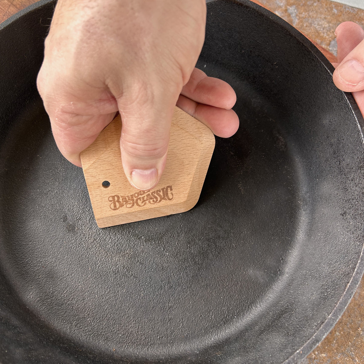 Person holding beech wood scrapper in a cast iron skillet