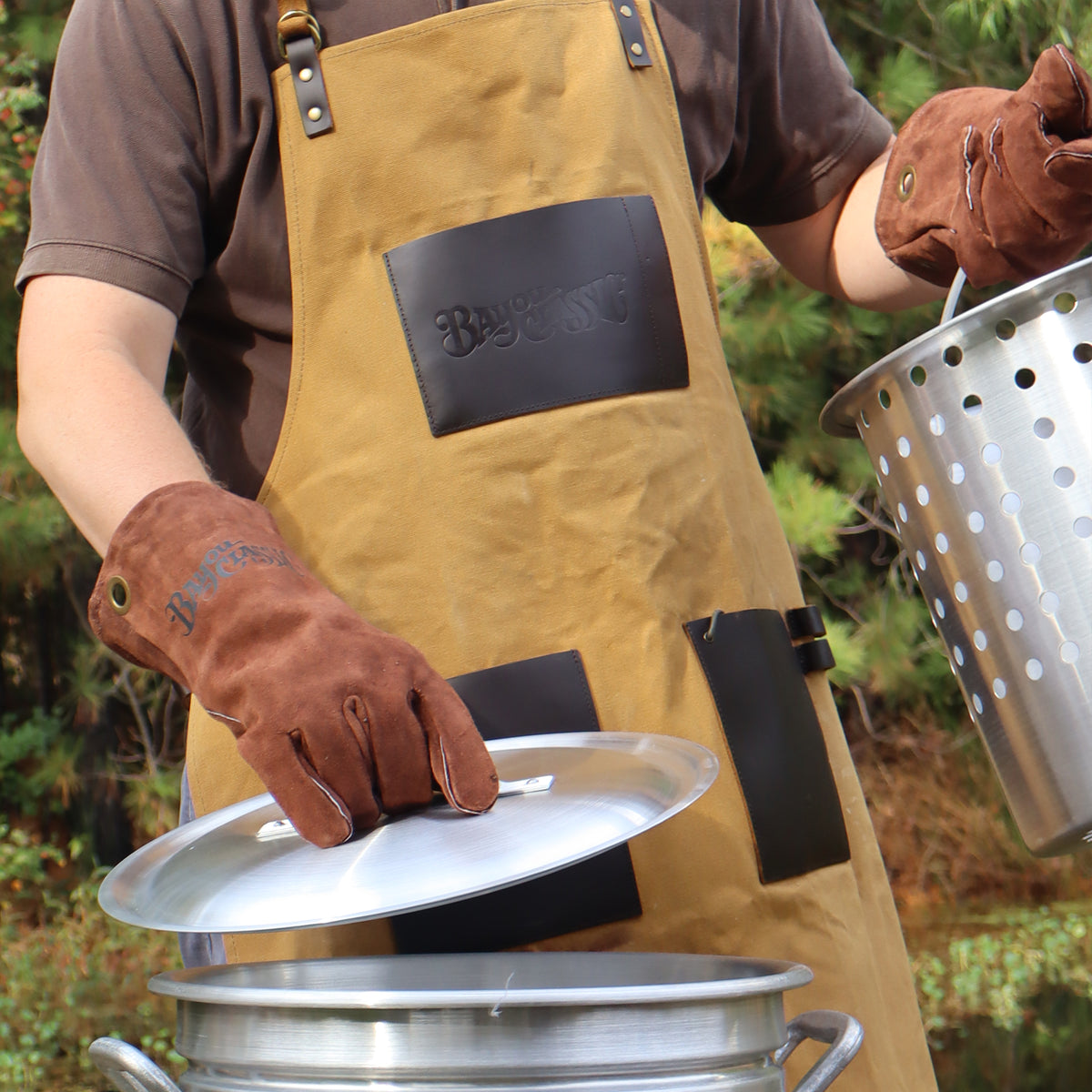 Person outside wearing an apron and using brown fry gloves with an aluminum stockpot 