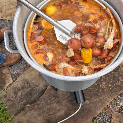 Low country boil with crab legs and vegetables using a stir paddle in an aluminum stockpot