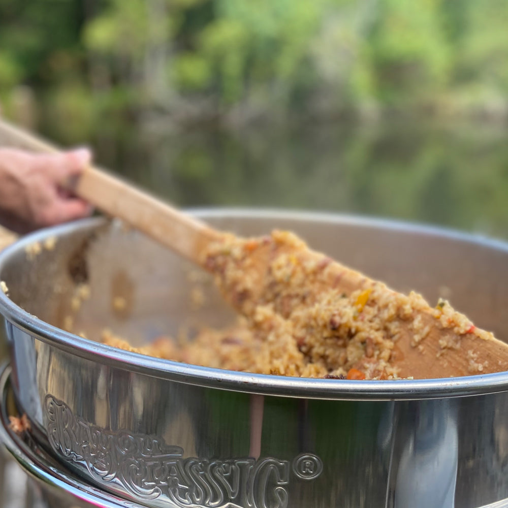 Stainless kettle with a rice dish being stirred with wooden spoon, outdoors