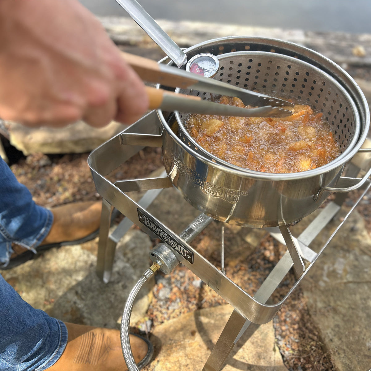 Person frying food outside in a stainless fry pot and cooker