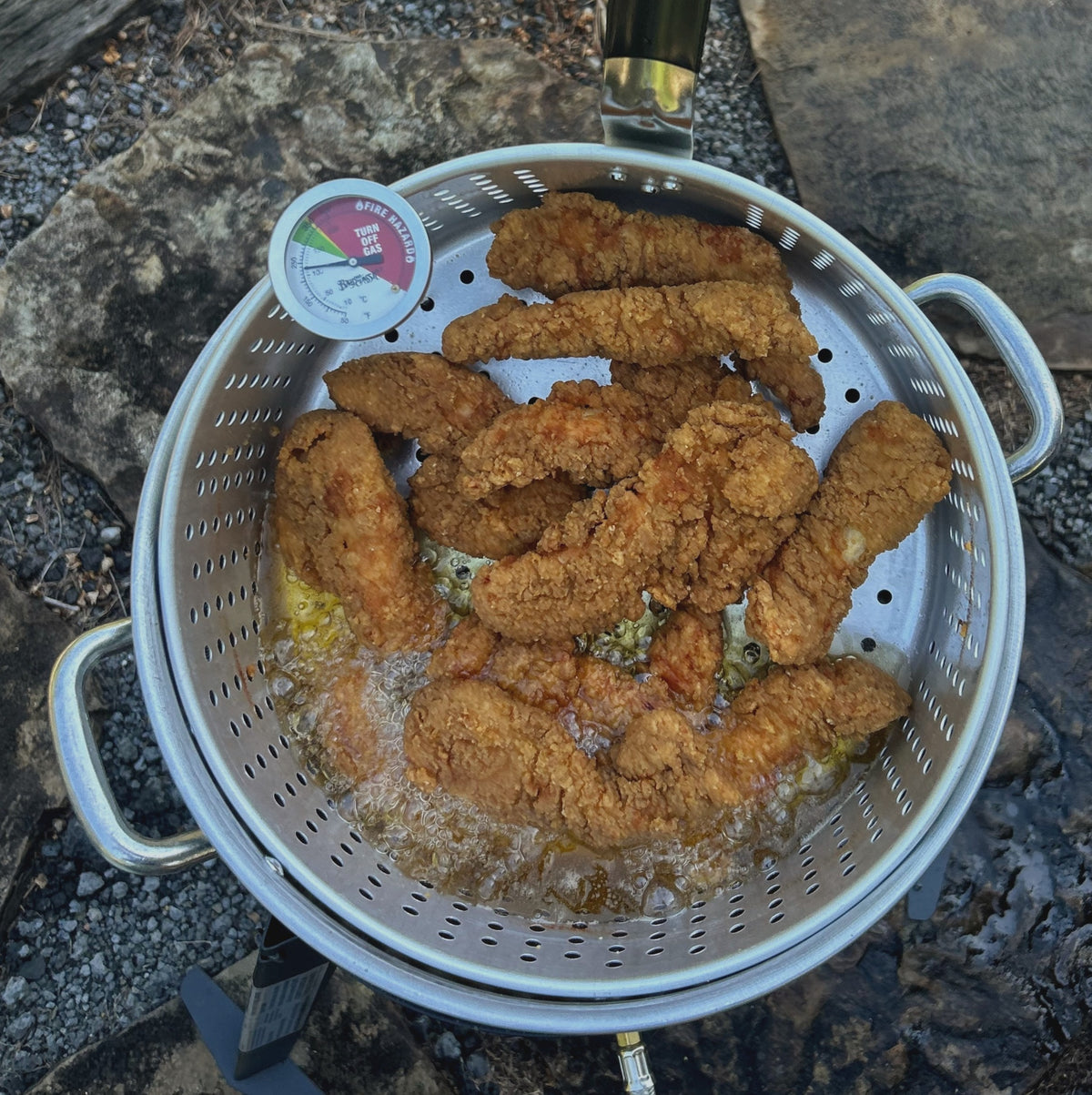 Fried chicken being fried in a fry pot on an outside surface.