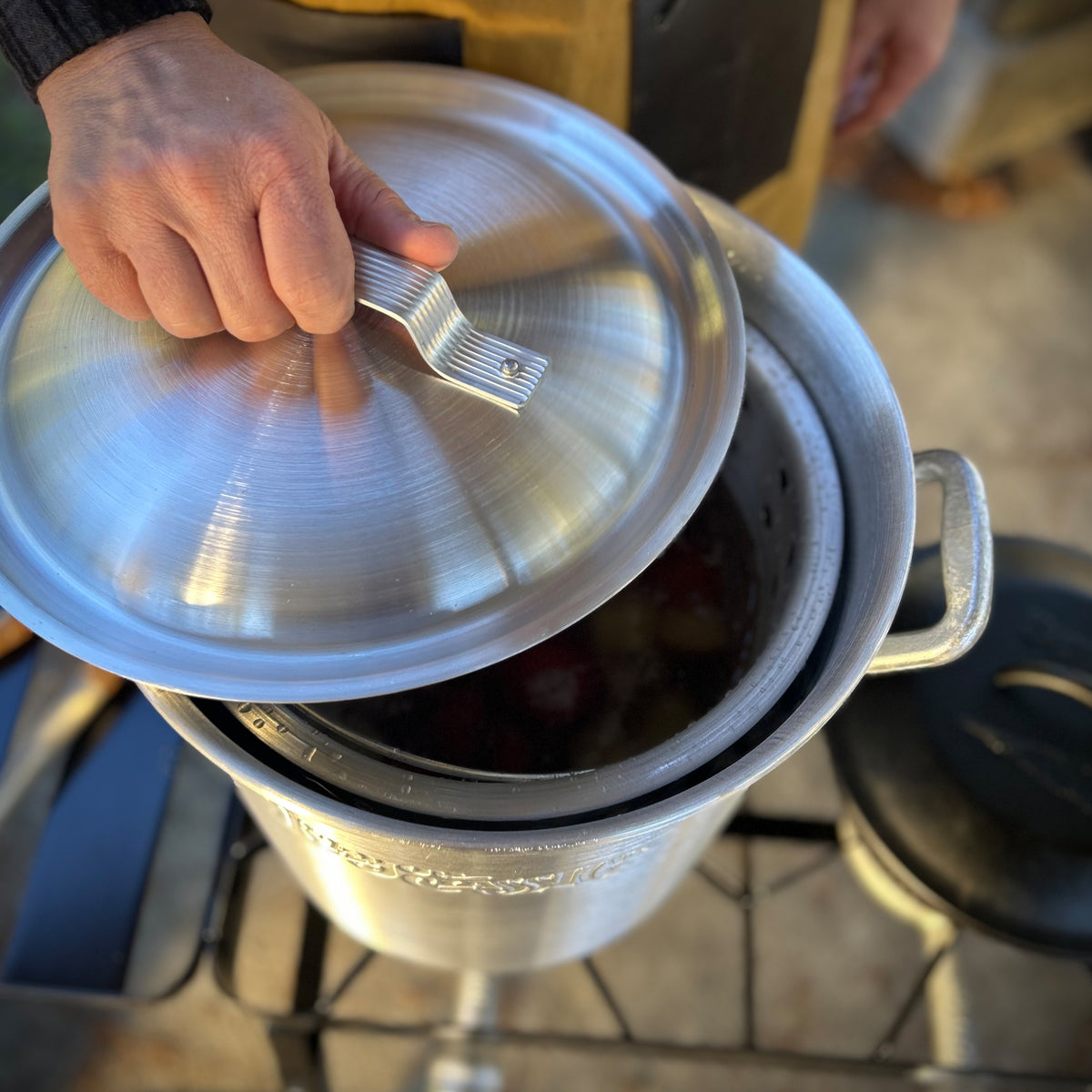 Person opening lid of an aluminum stockpot outside on an outdoor cooker