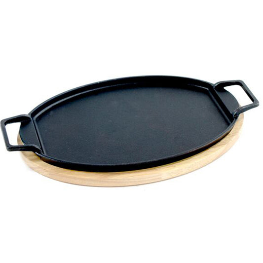 A large black cast iron oval fajita pan with loop handles on a wooden trivet on a white background