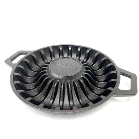A black cast iron shrimp pan with ridged pattern to hold shrimp and two handles on a white background
