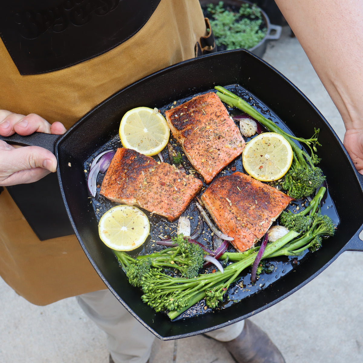 Person holding cast iron square skillet with cooked fish and broccolini