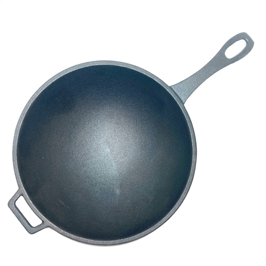 A top view of a black cast iron wok with a helper handle on a white background