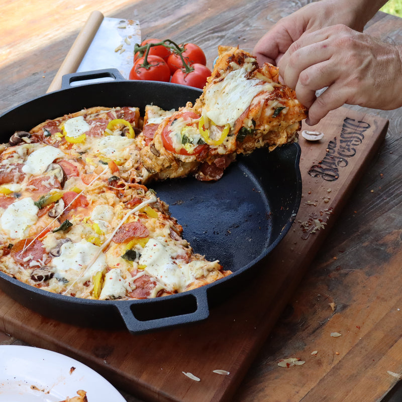 Person getting a piece of pizza from a large cast iron skillet