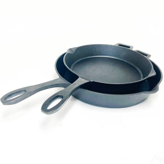 A set of two black cast iron skillets, one inside the other on a white background