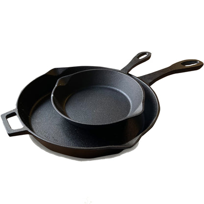 A set of two black cast iron skillets, one larger than the other, with pour spouts and handles on a white background.