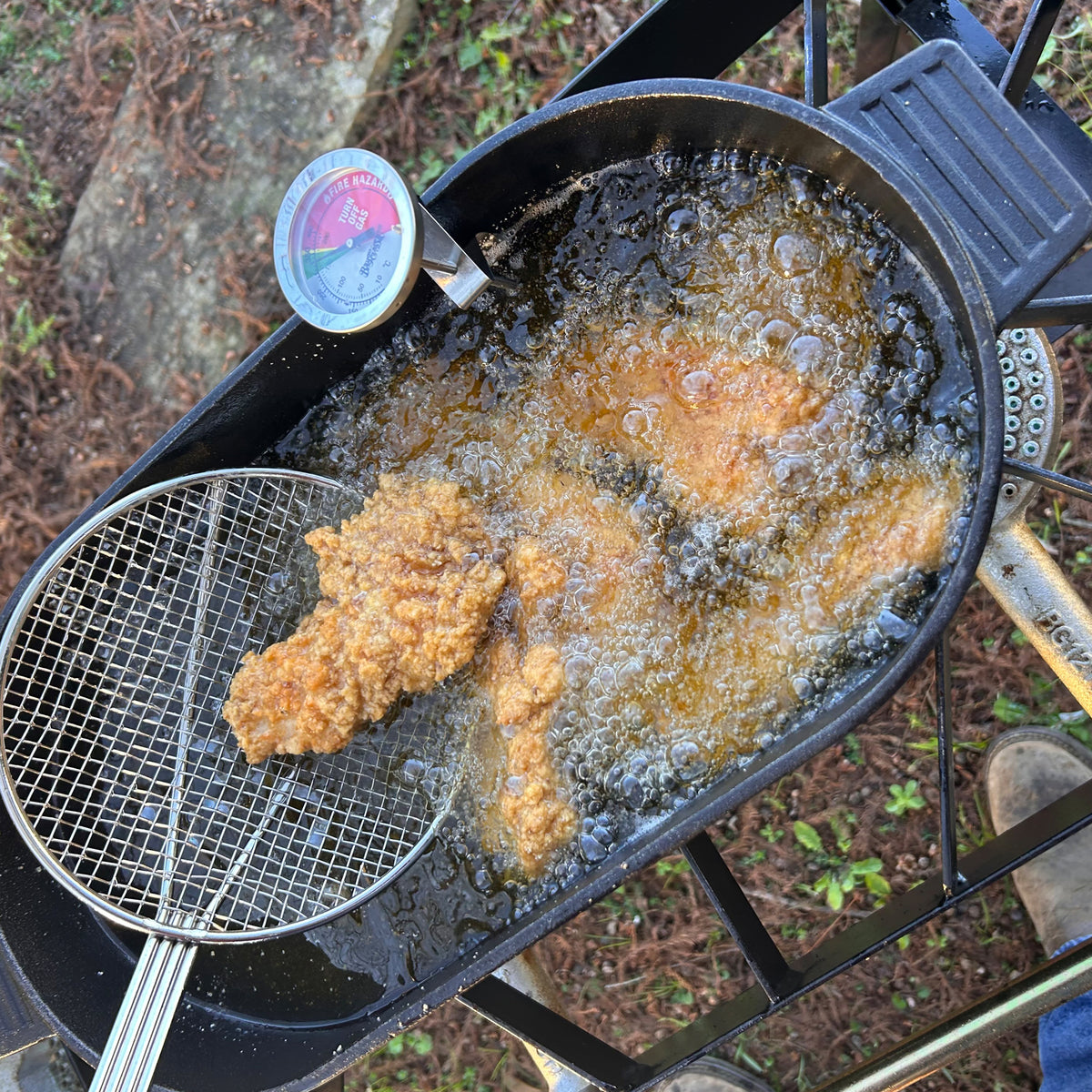 Cast Iron Oval Fryer frying chicken outside using a skimmer