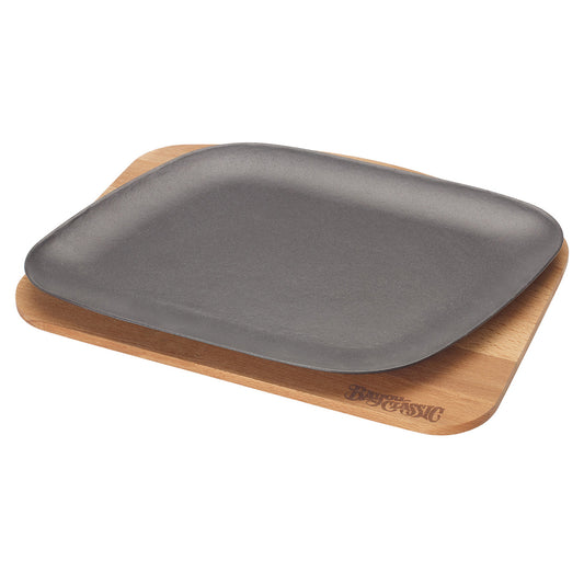 A black enameled cast iron fajita pan placed on a wooden trivet on a white background