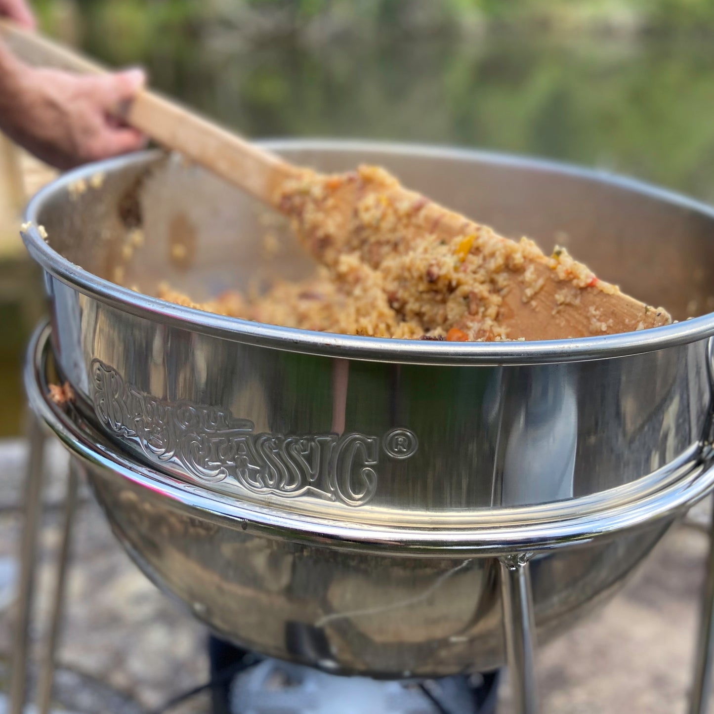 Stainless Kettle with cooked jambalaya and a wooden stir paddle in an outdoor setting
