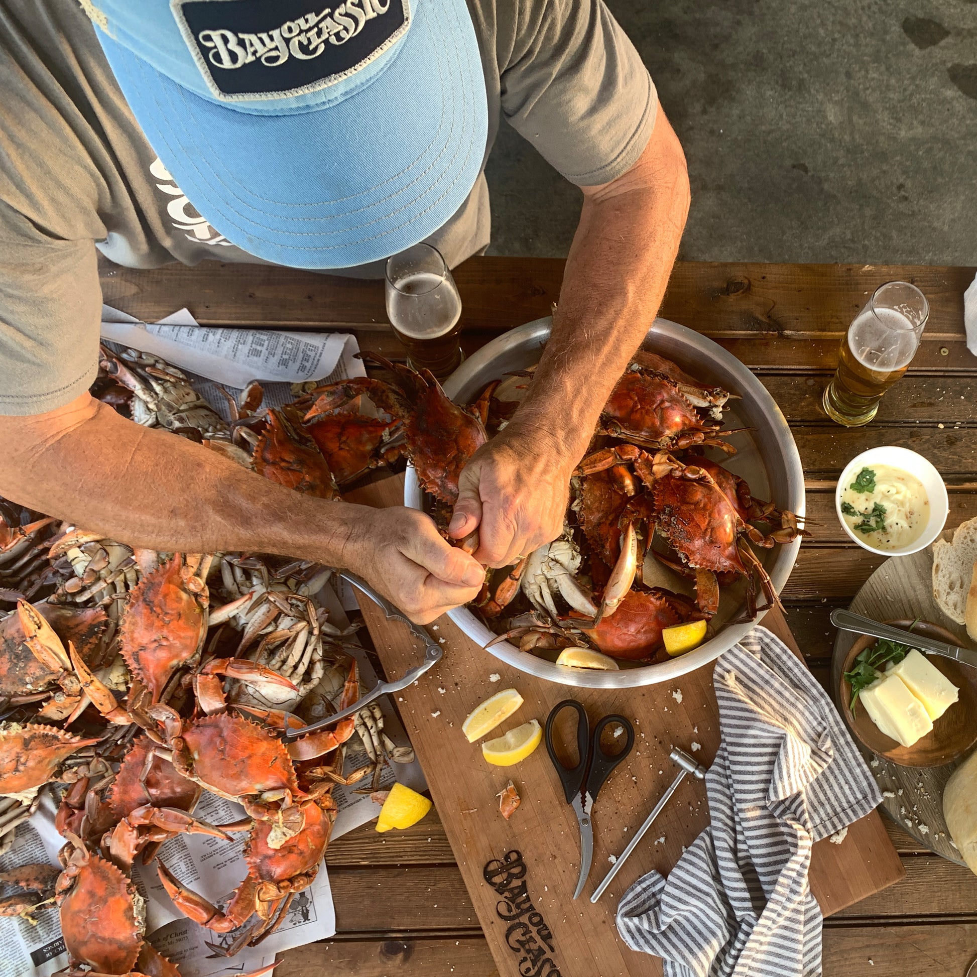 Person eating crabs at a picnic table with utensils, a serving tray and lemon wedges.