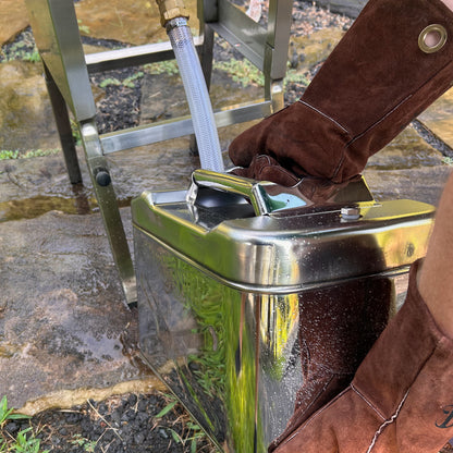 Person wearing brown leather fry gloves using a jerry oil can outdoors on a stone surface