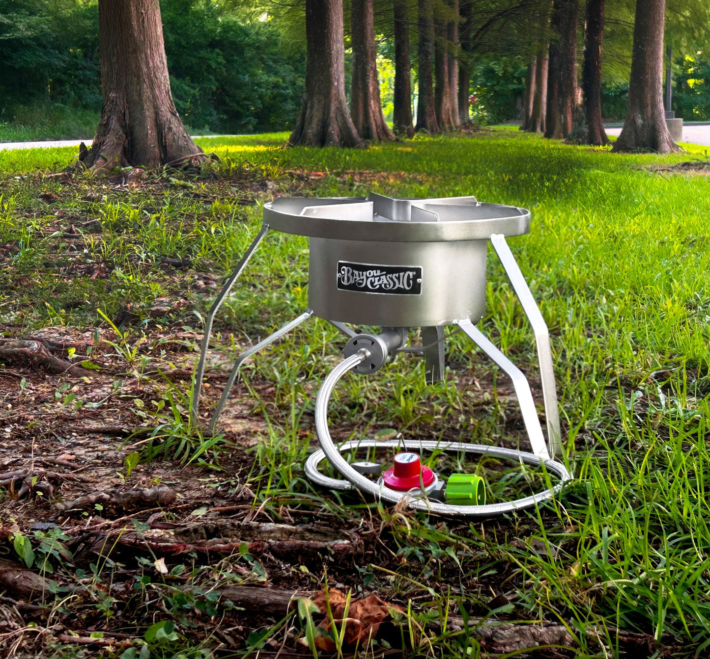 A stainless outdoor cooker set in the grass with a row of trees.