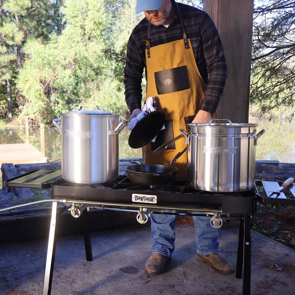 Person using a triple burner cooker outside with two stockpots and a cast iron skillet