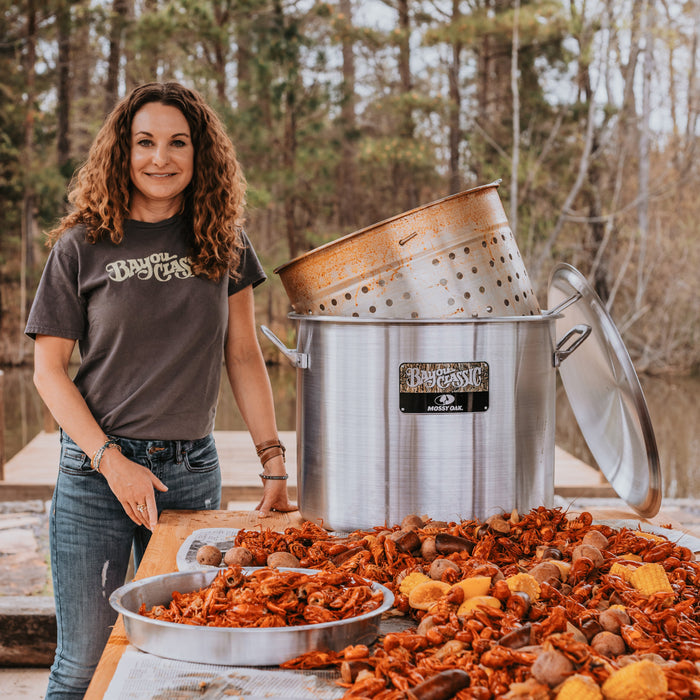 Woman standing behind a table with roasted corn and other food items outdoors.