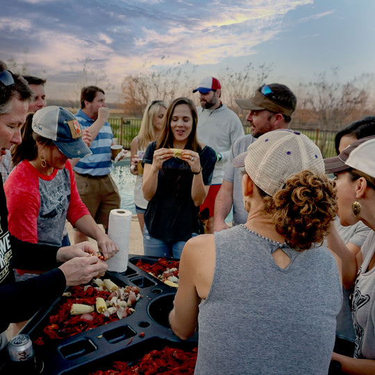 Group of people preparing food at a picnic table outdoors with a scenic background