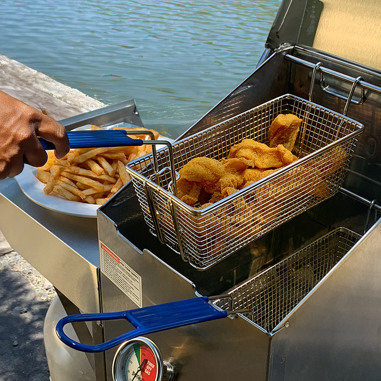 Fried chicken and french fries being served from a deep fryer by a body of water.