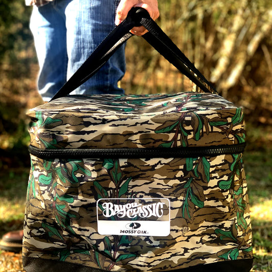 Mossy Oak Greenleaf pattern camouflage gear bag with 'Bayou Classic' logo held by a person outdoors. 