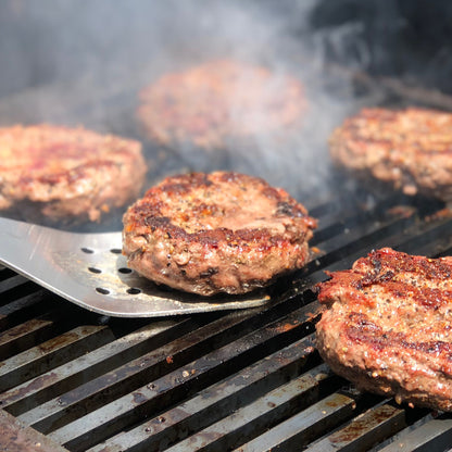 Stainless spatula flipping hamburgers cooking on a grill with smoke