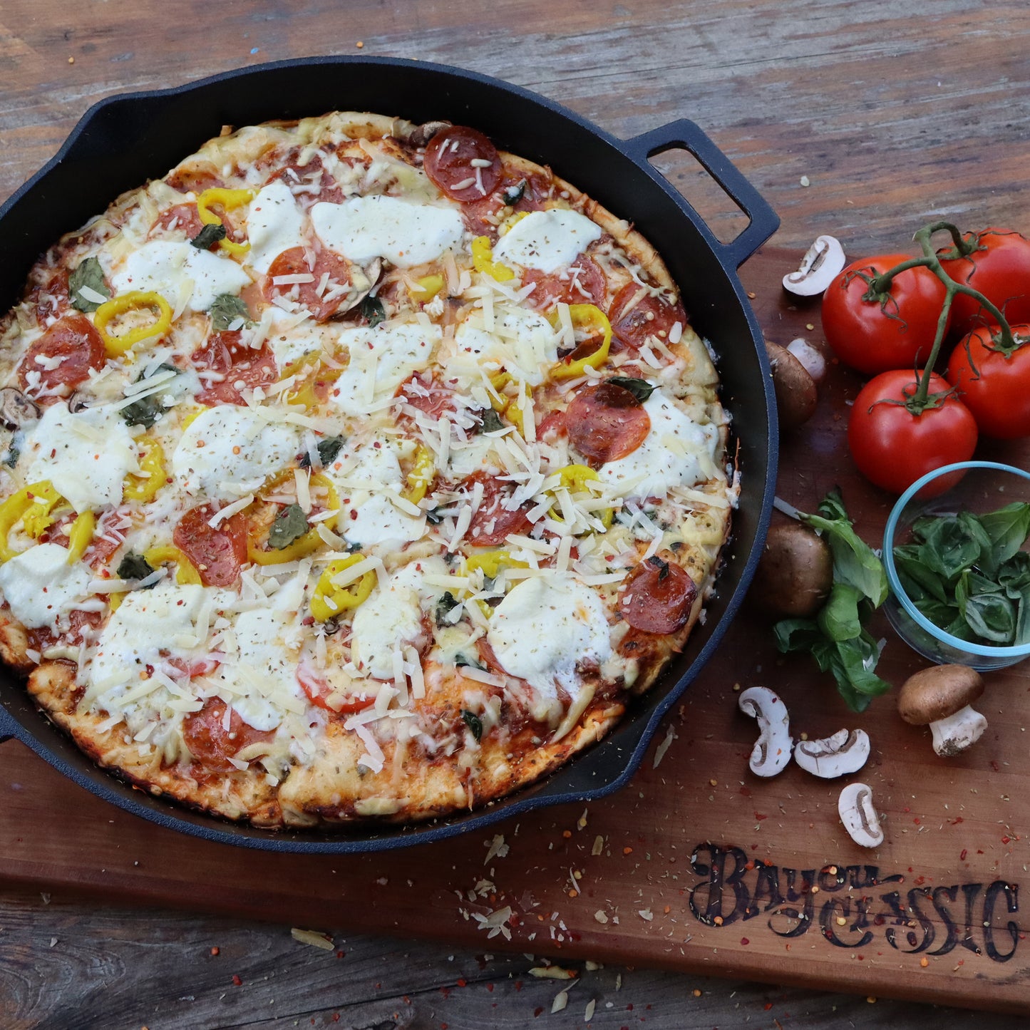 Personal-sized pizza in a cast iron skillet on a wooden board with fresh ingredients.