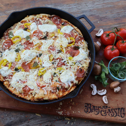 Personal-sized pizza in a cast iron skillet on a wooden board with fresh ingredients.