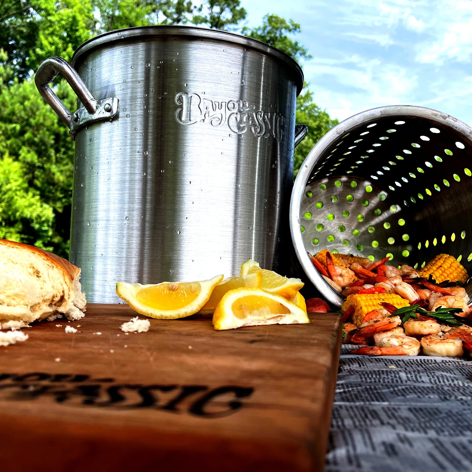 Aluminum Stpckpot and basket outside with boiled shrimp, lemon wedges, and french bread.