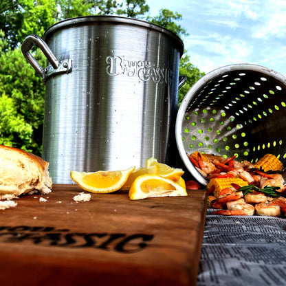 Aluminum Stpckpot and basket outside with boiled shrimp, lemon wedges, and french bread.