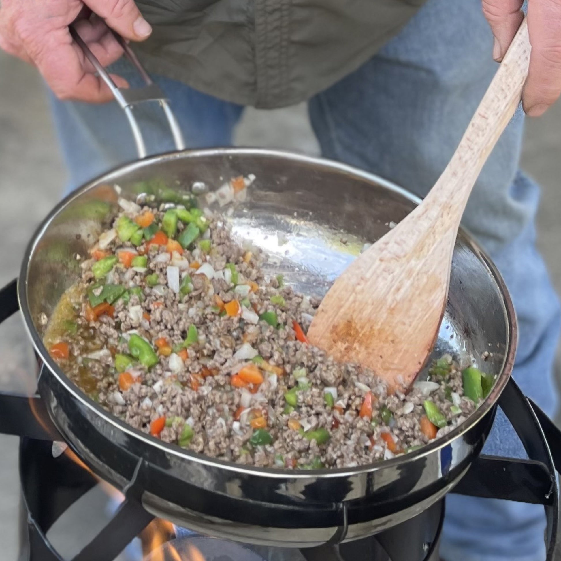 Person cooking ground meat with vegetables in a stainless steel pan using a wooden roux spoon.