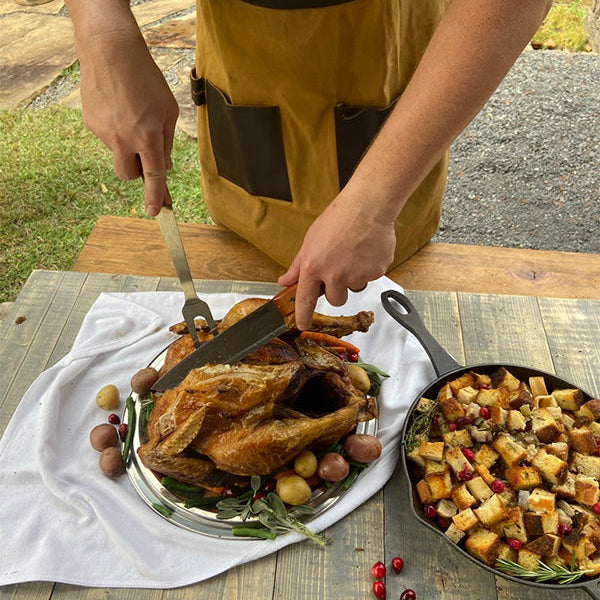 Man carving turkey next to a cast iron skillet of cornbread dressing