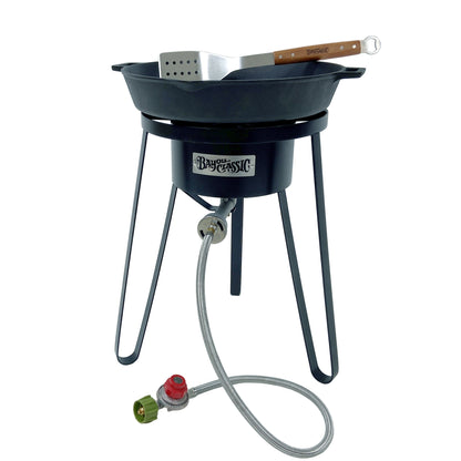 21-in tall steel cooker with 16-in double handled skillet and a spatula on a white background.
