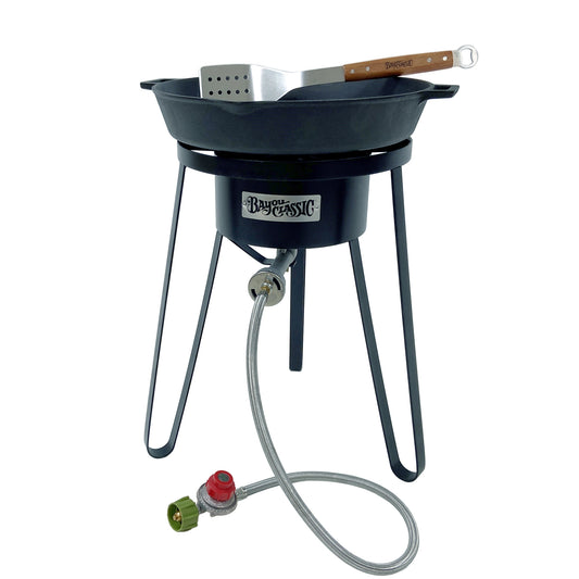 21-in tall steel cooker with 16-in double handled skillet and a spatula on a white background.