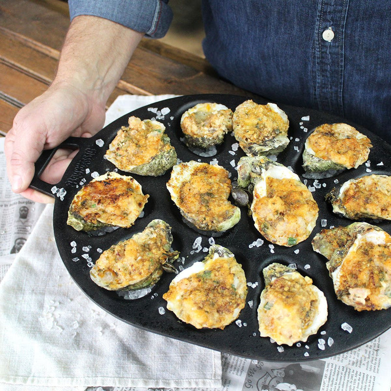 Person holding a cast iron oyster pan with chargrilled oysters and rock salt