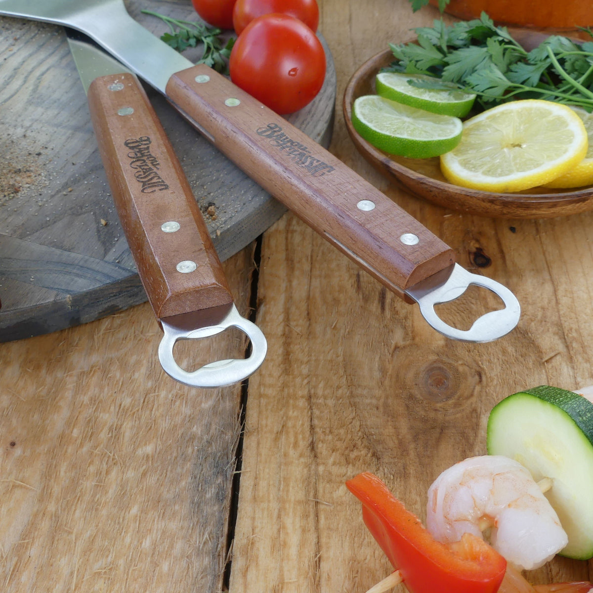 The bottle opener end of the spatula and tongs on a wood surface with vegetables.