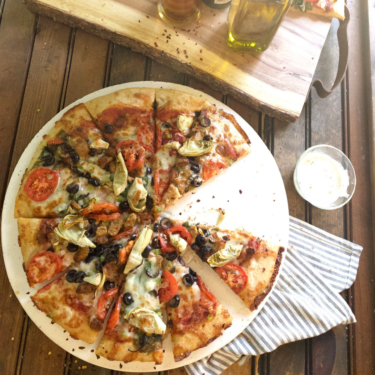 Cooked pizza on a ceramic pizza stone sitting on a wood surface